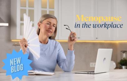 A woman sitting at her laptop cooling herself with a fan.