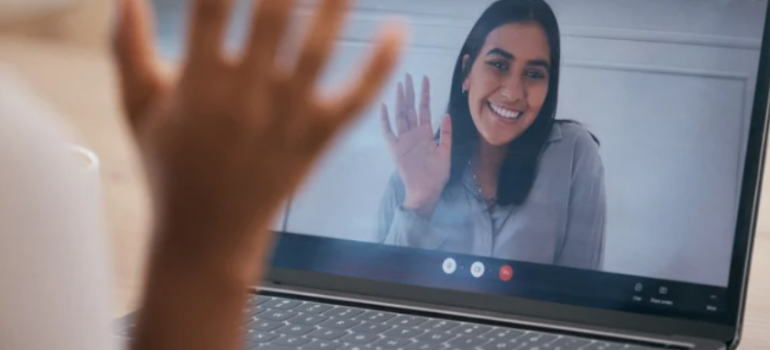 A woman on a computer screen waving and a hand waving in response.